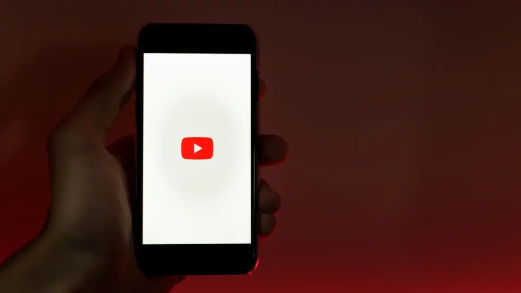 A person holding a smartphone on a red background with the YouTube logo on its screen. Illustrates [alt text].