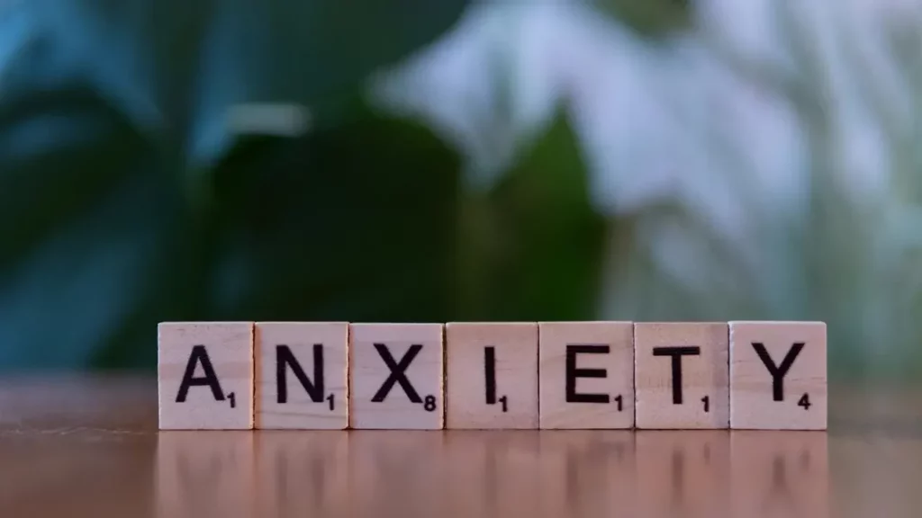 A wooden block spelling the word anxiety on a table. Themes of social anxiety.