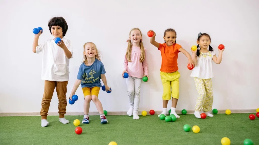 Five children against a wall throwing toys