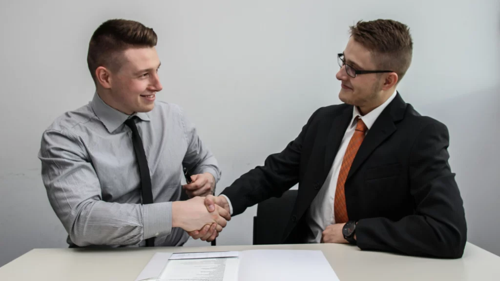 Two men facing each other while shake hands and smiling. Themes of transferable license.