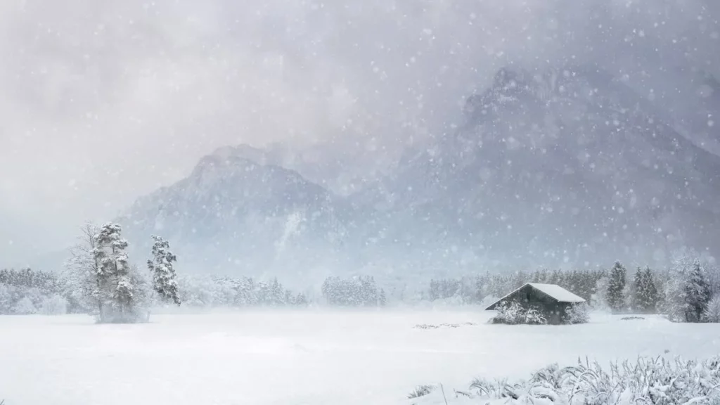 Photo of a winter scene with heavy snow on a field with a hut in the midground and big mountains in the background.